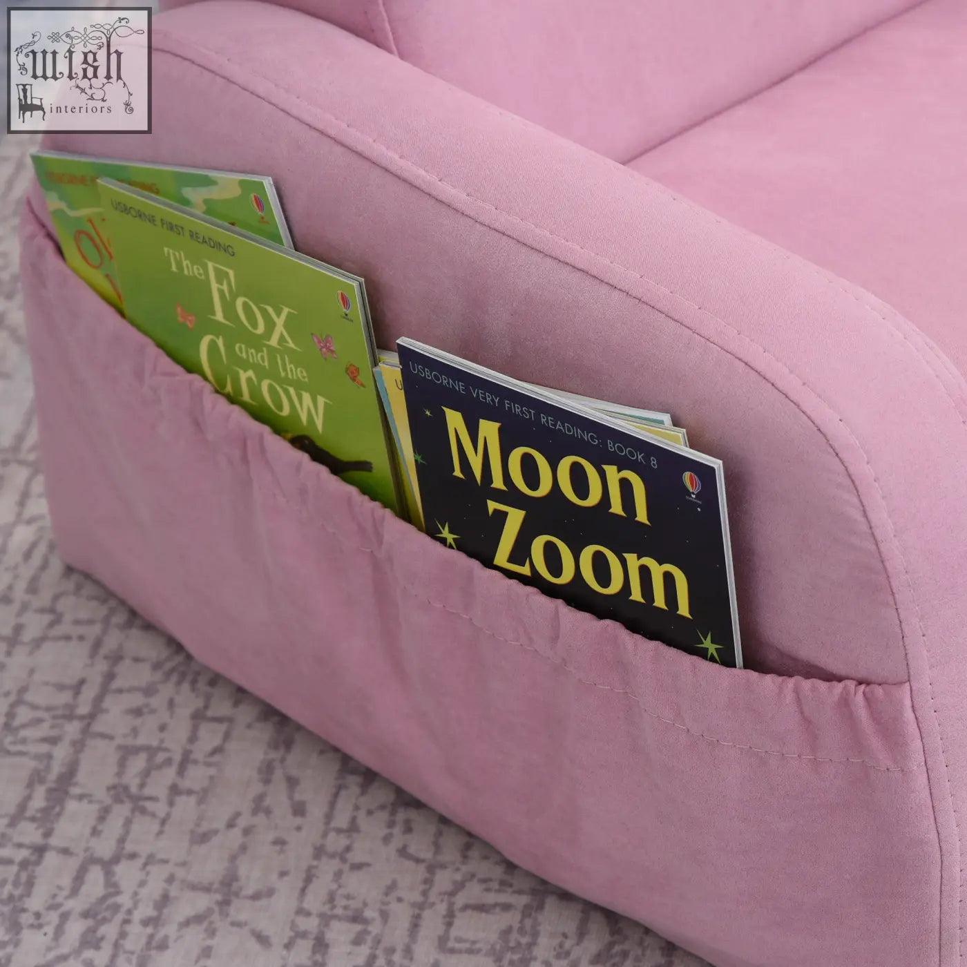 Pink kids armchair sofa bed with wood frame and built-in book pocket holding two usborne first reading books