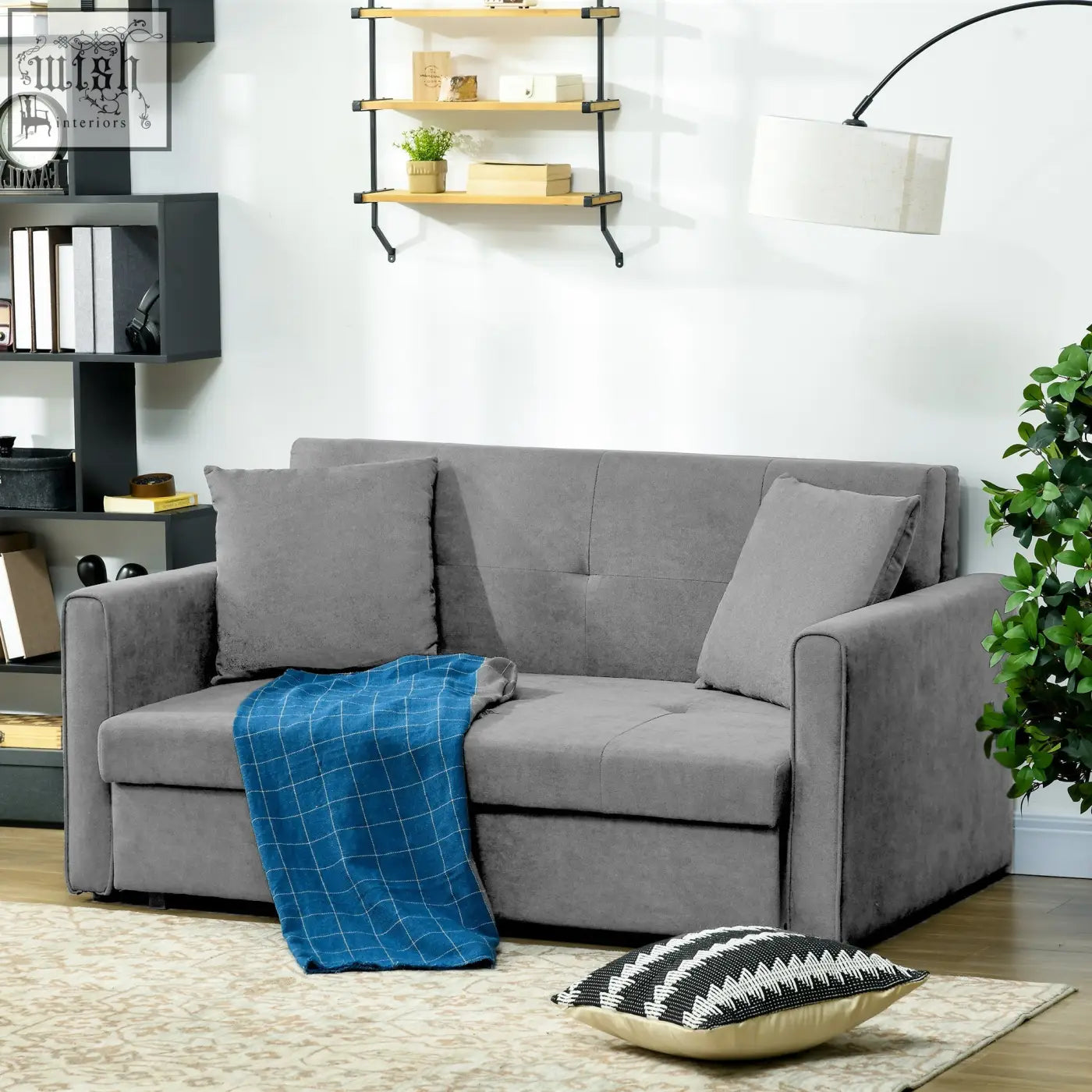 Light grey fabric seater sofa bed with tufted back, matching pillows, and blue plaid blanket for living room use