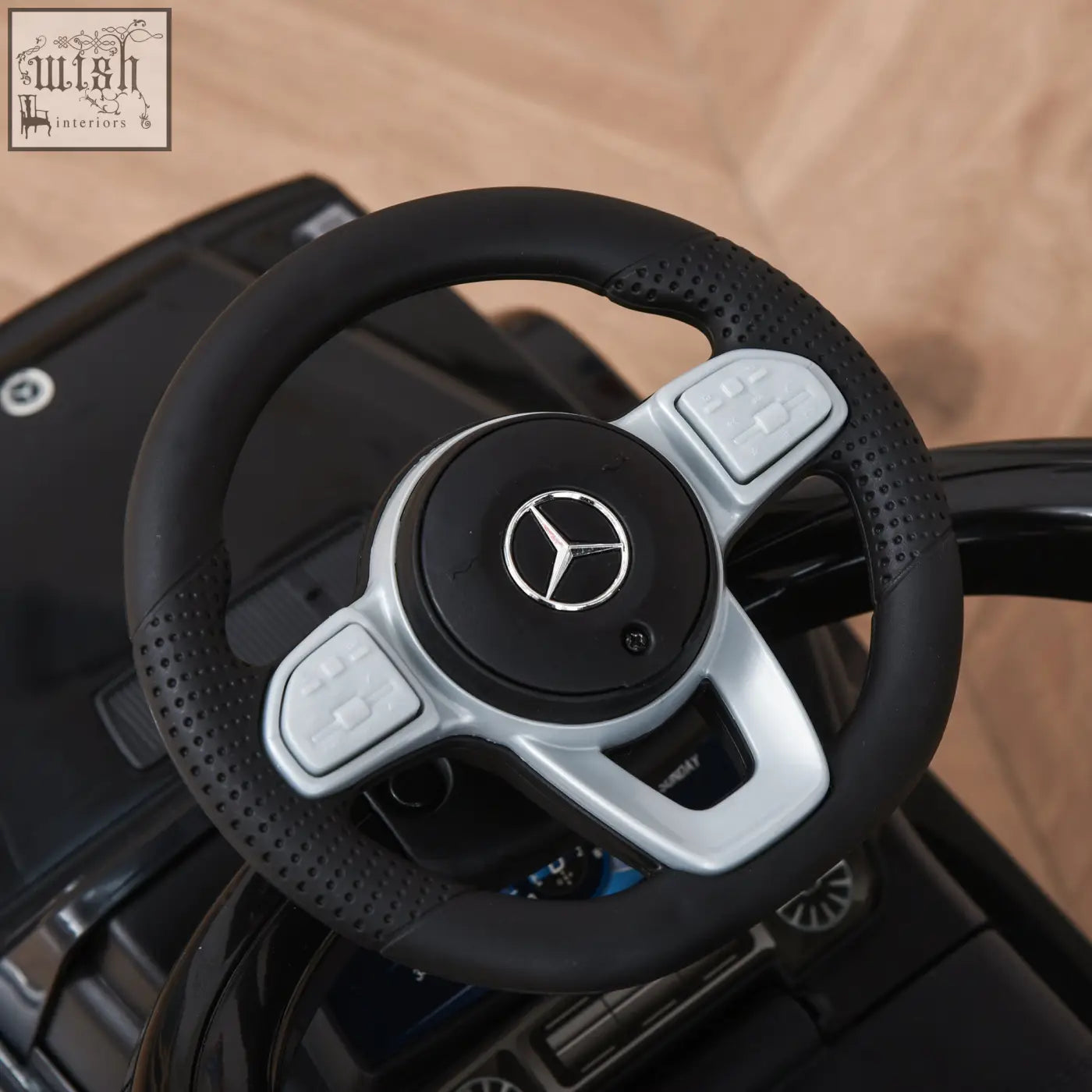 Black and silver mercedes-benz branded steering wheel with perforated grip and control buttons on kids sliding car