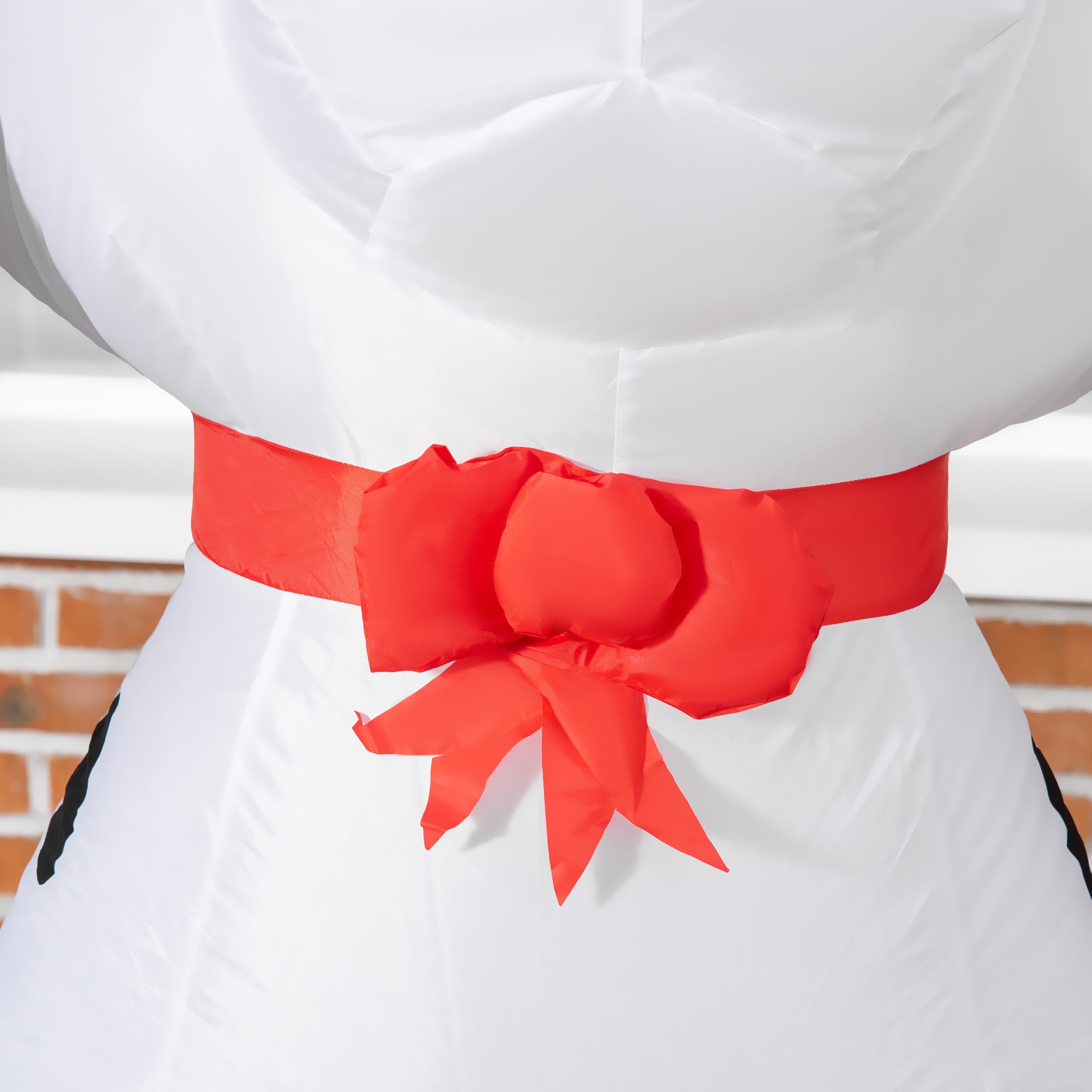 A vibrant red satin ribbon tied around the waist of a white and black inflatable cow made of resistant polyester cloth