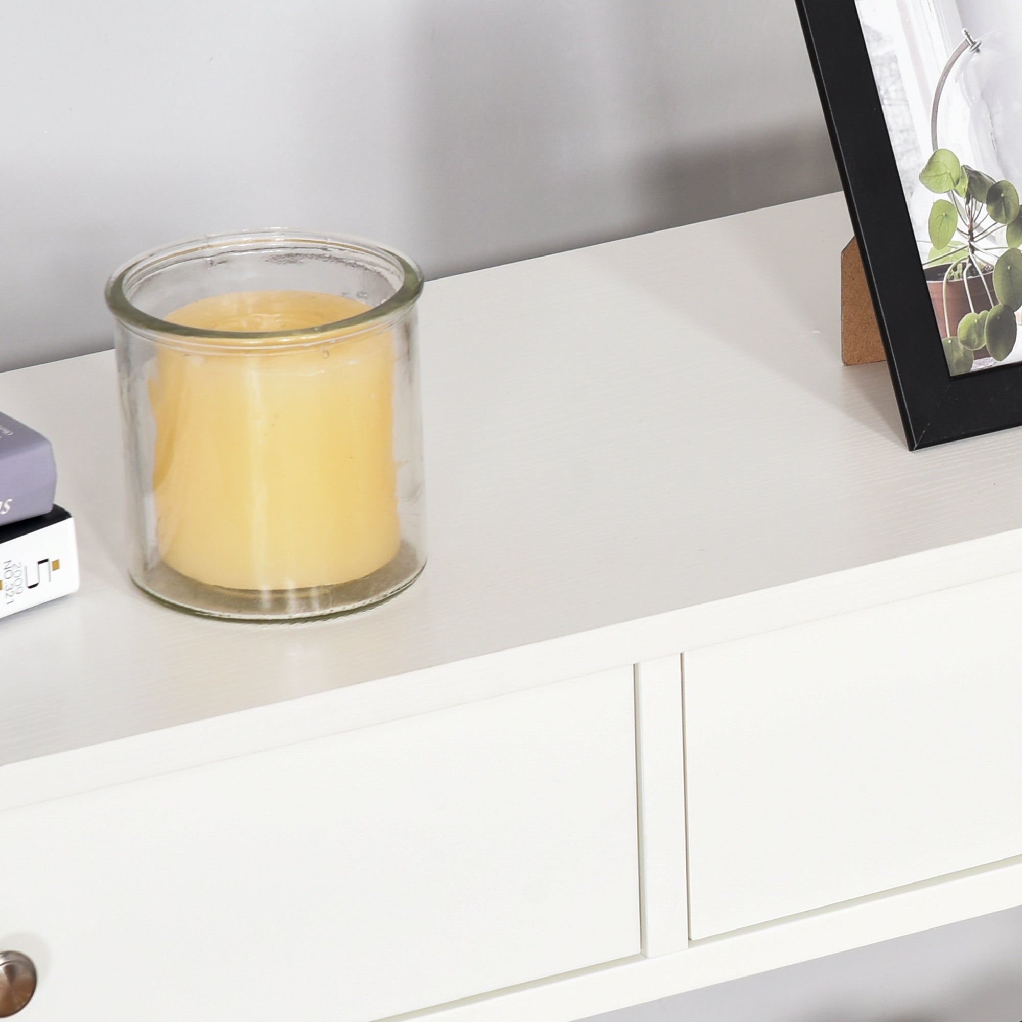 Clear glass candle holder with solid yellow candle on white homcom console table featuring two drawers and shelves