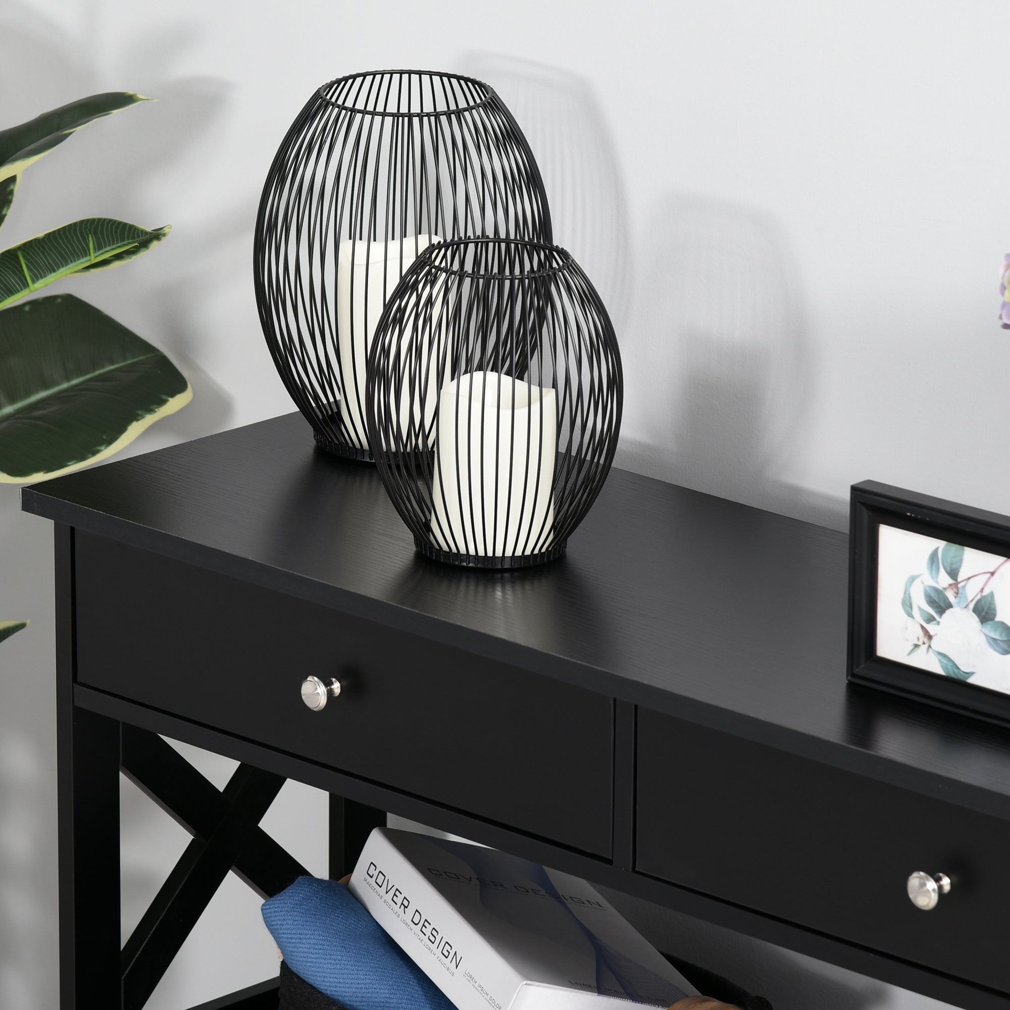 Black wireframe candle holders with white candles on a black console table with two drawers and x support frame