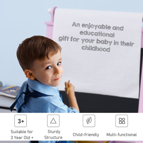 A young boy holds chalk beside a pink homcom wooden kids easel with paper roll chalkboard and storage baskets