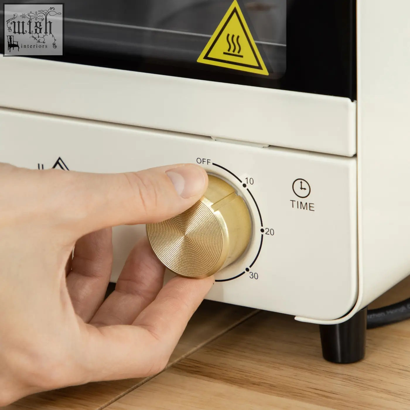 A hand adjusts the gold-toned dial on a cream white homcom mini oven with crumb tray and baking tray features