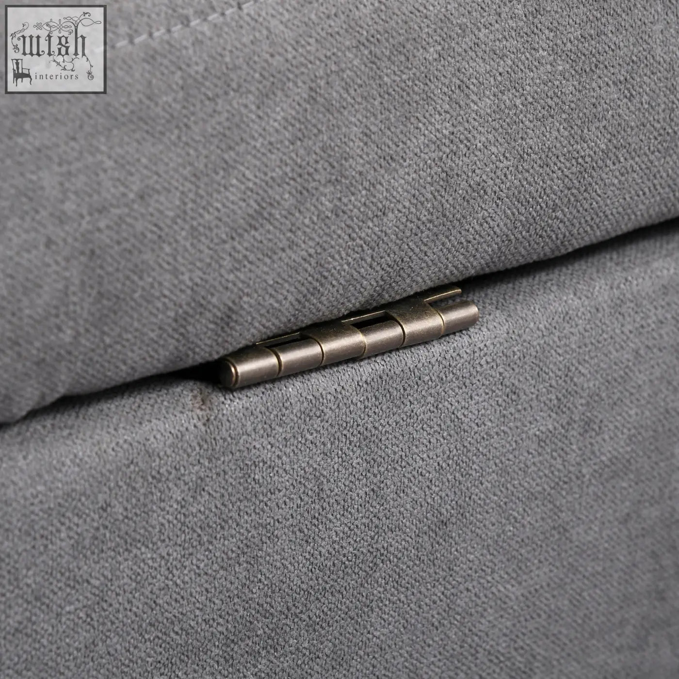 A metallic hinge with a brushed finish embedded in gray fabric seam on a grey seater sofa with eucalyptus wood legs ensure stability