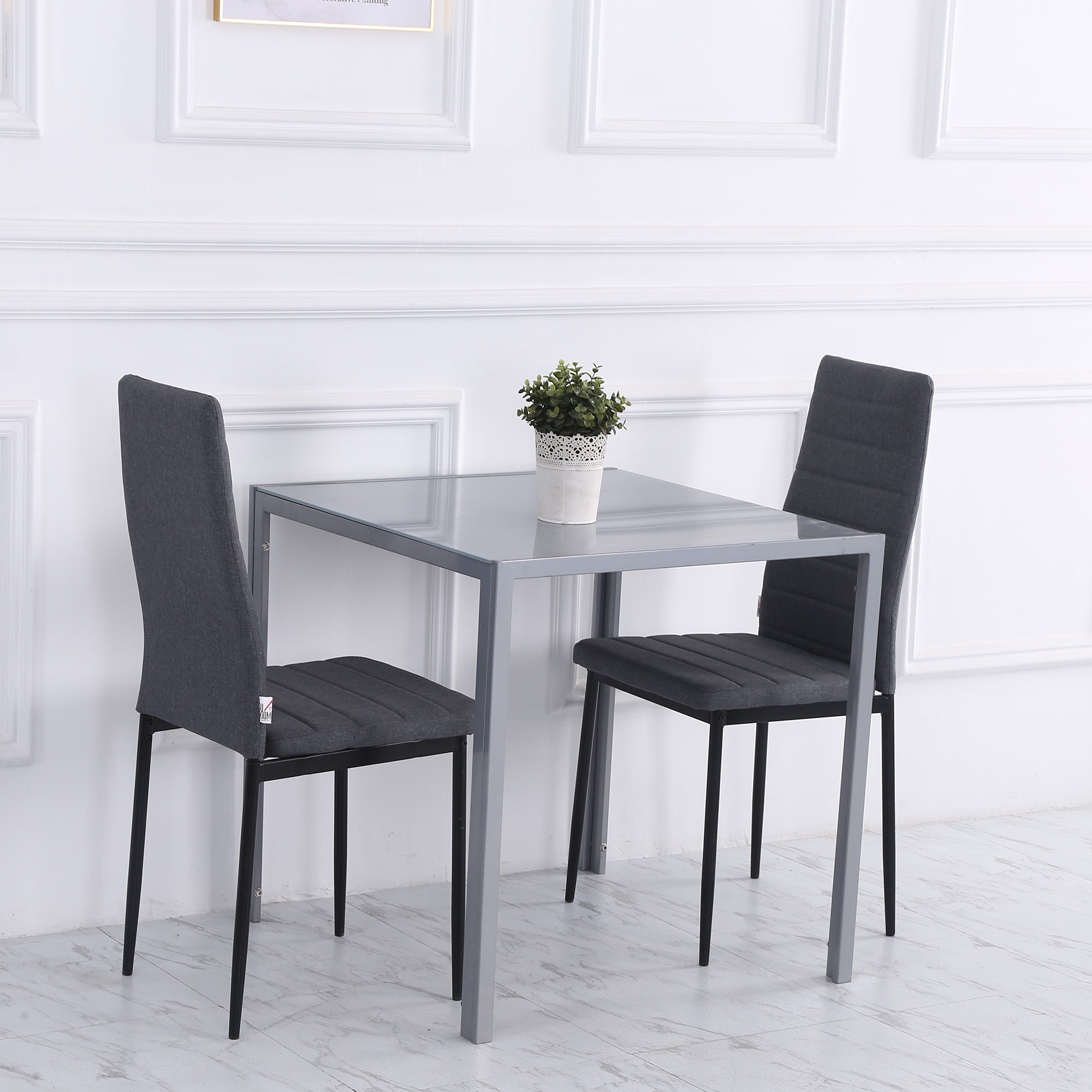 Gray glass-top dining table with powder coated steel legs and two gray upholstered chairs for dining room use