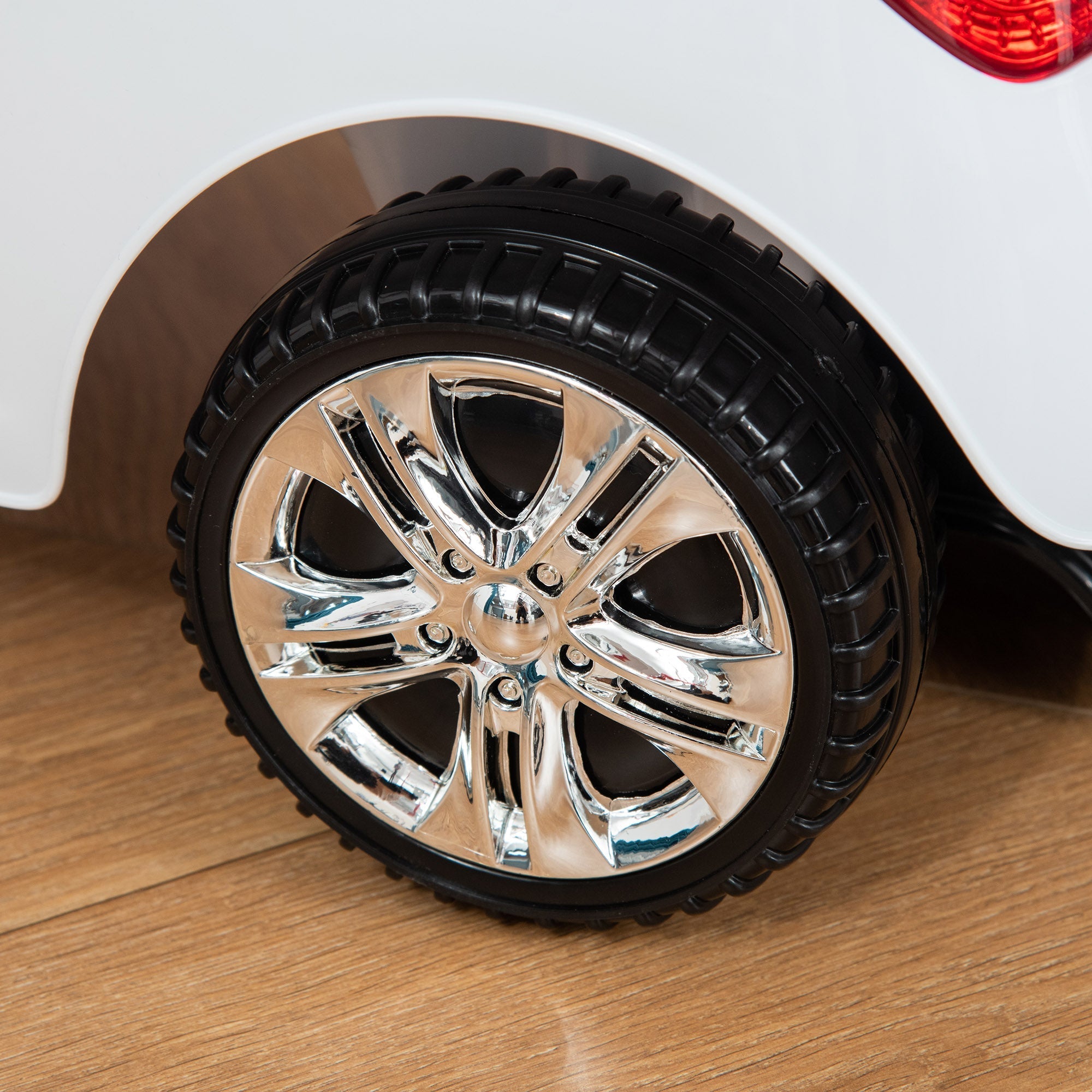 Close up of chrome multi-spoke alloy wheel with black tire on white homcom ride on car with sliding car feature