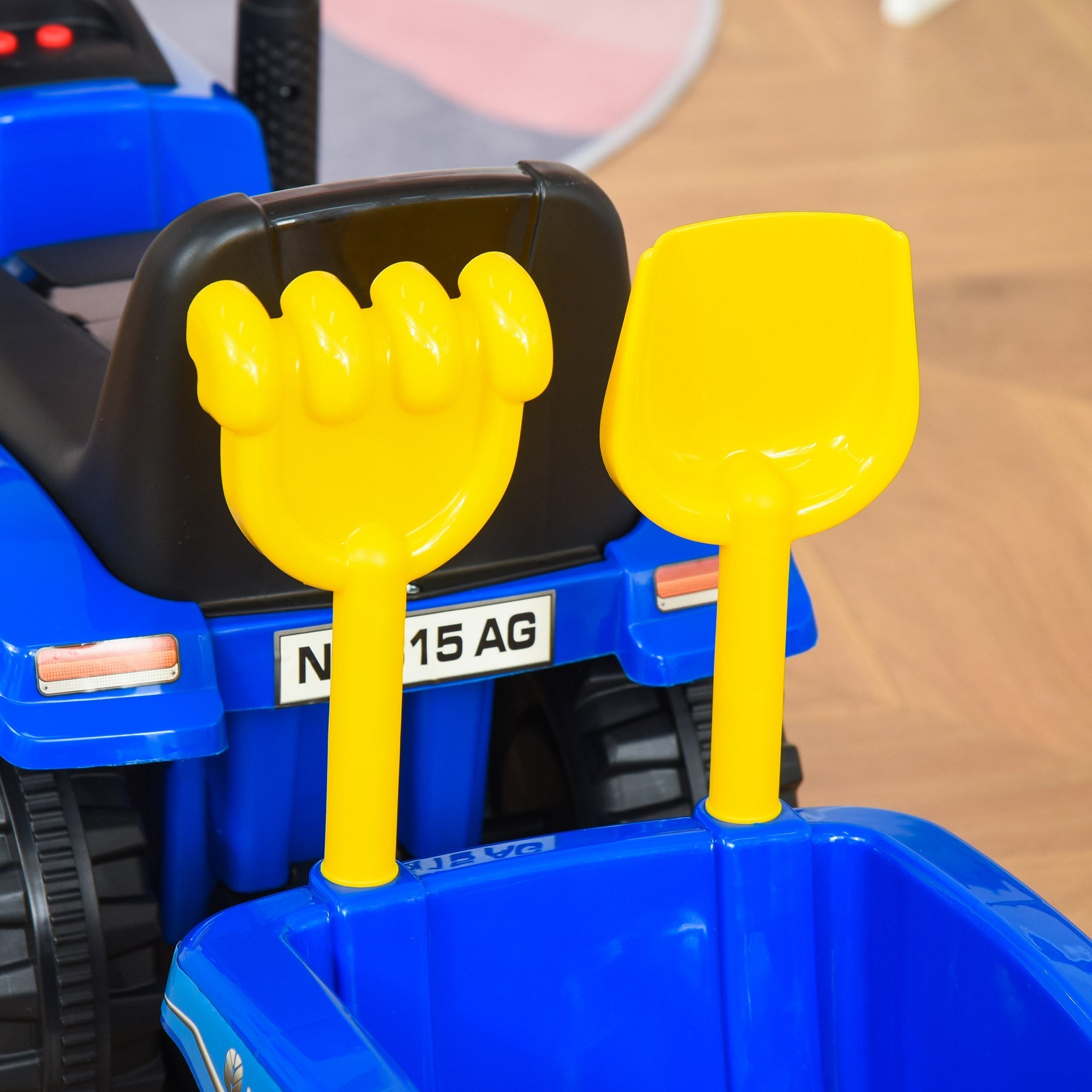 Bright yellow plastic shovel and rake set on blue homcom ride on tractor with steering wheel and cargo box for toddlers