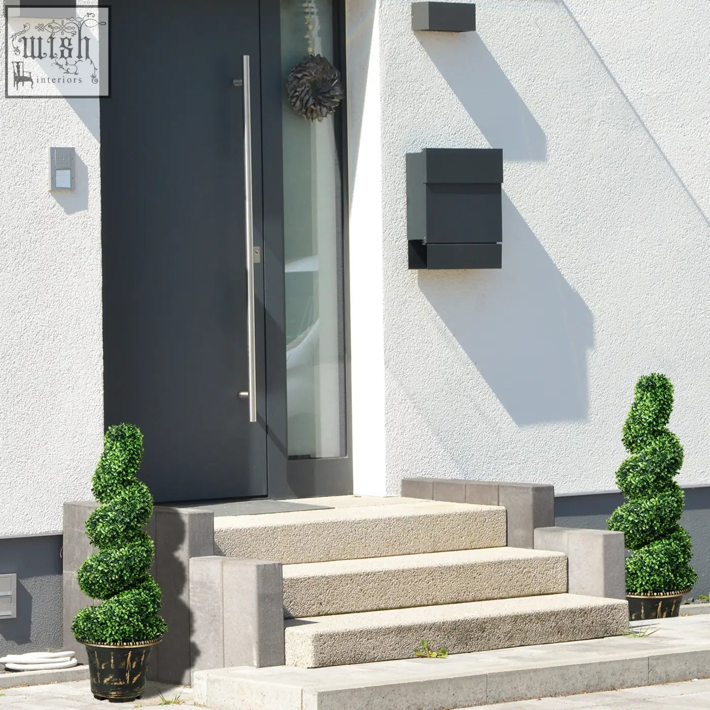 Black modern mailbox mounted on white stucco wall near homcom spiral boxwood trees artificial topiary decor