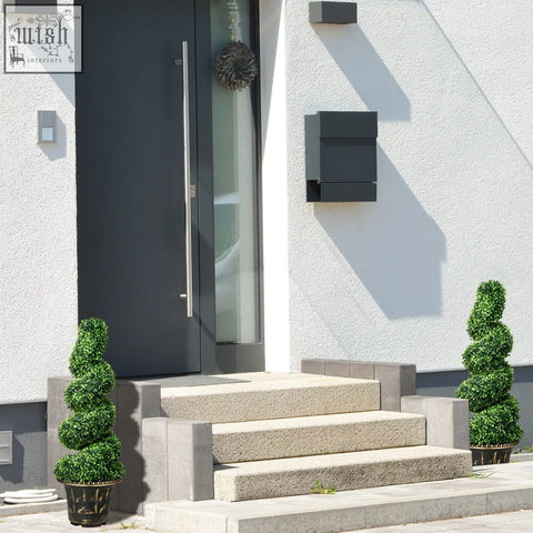 Black modern mailbox mounted on white stucco wall near homcom spiral boxwood trees artificial topiary decor