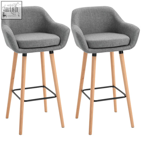 Gray upholstered bar stools with solid wood legs and black metal footrests featuring linen upholstery for dining room use