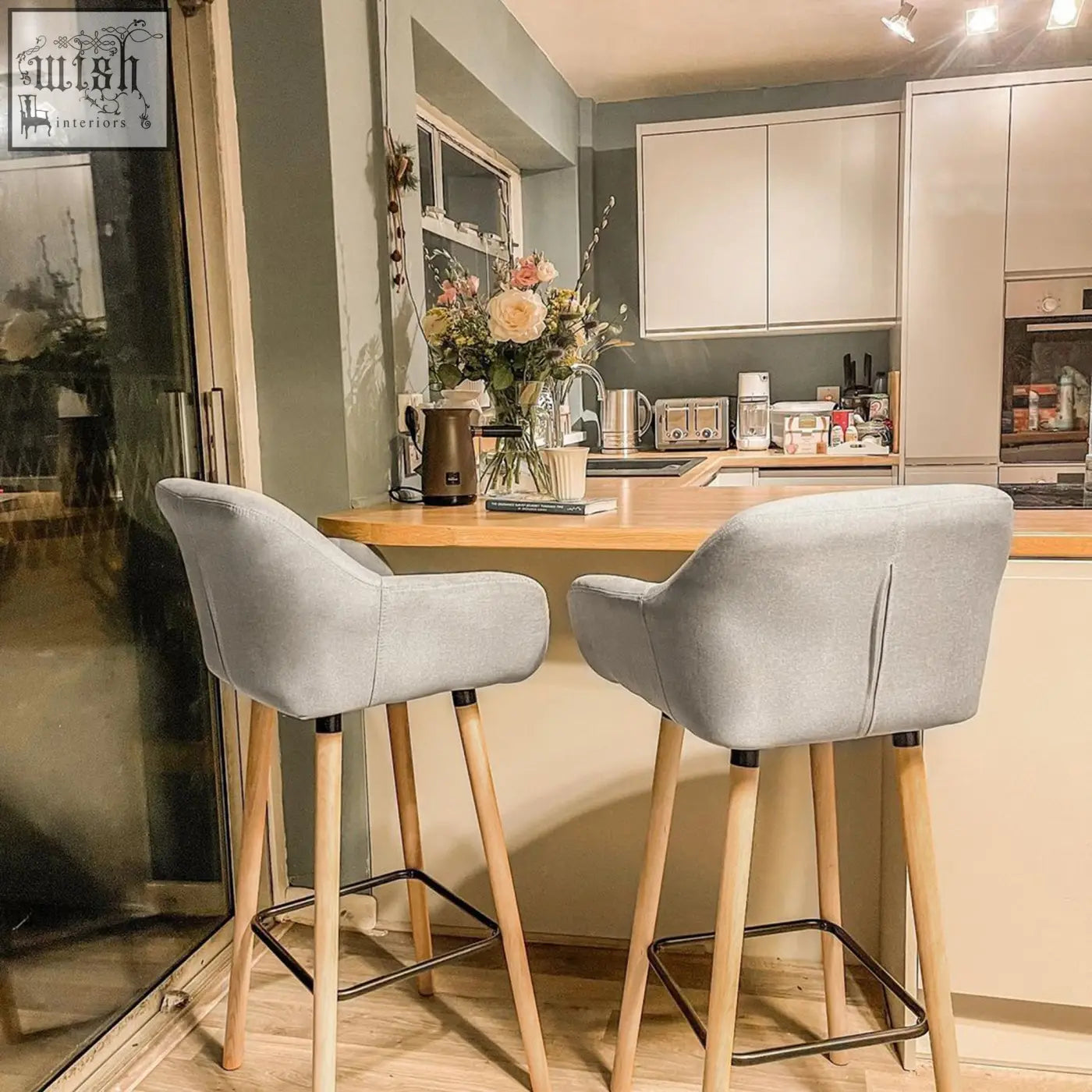Two modern grey linen upholstery bar stools with solid wood legs and black metal footrests for living room or dining room