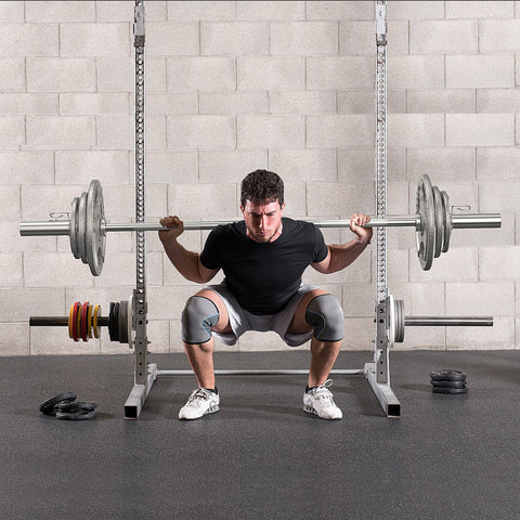A man squats with a barbell on a power rack using homcom cast iron weight plates with a 2 inch centre hole