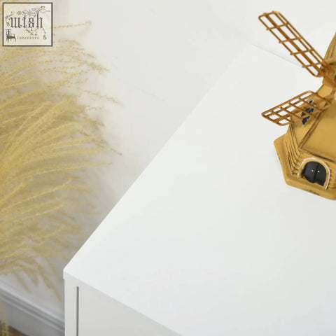 Golden windmill figurine with intricate lattice blades on a hexagonal base beside homcom 4-drawer dresser with clean white design and hairpin-shaped metal legs