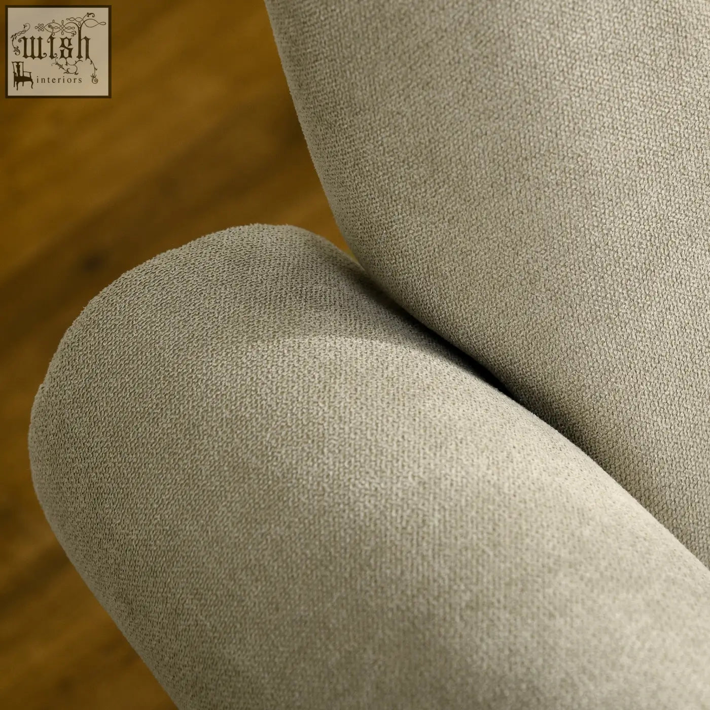 Beige upholstered accent chair with soft woven fabric, curved arms, thick padding, and sturdy wooden frame legs