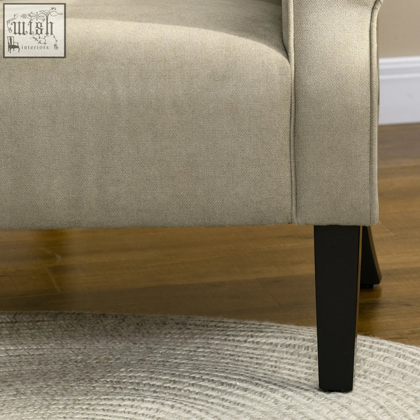 Beige upholstered accent chair with soft thick padding, curved arms, and wooden frame with sleek black legs