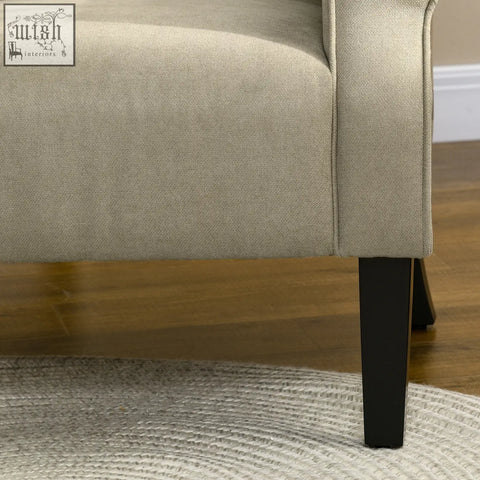 Beige upholstered accent chair with soft thick padding, curved arms, and wooden frame with sleek black legs