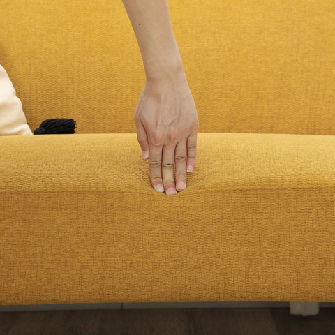 A hand rests on a mustard yellow velvet feel fabric 2 seater sofa with 21cm padded seat and solid rubberwood legs