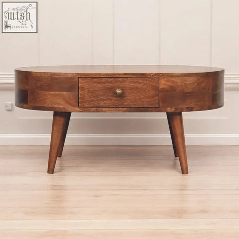 A sleek oval coffee table with a honey caramel finish and tapered legs in rich dark wood