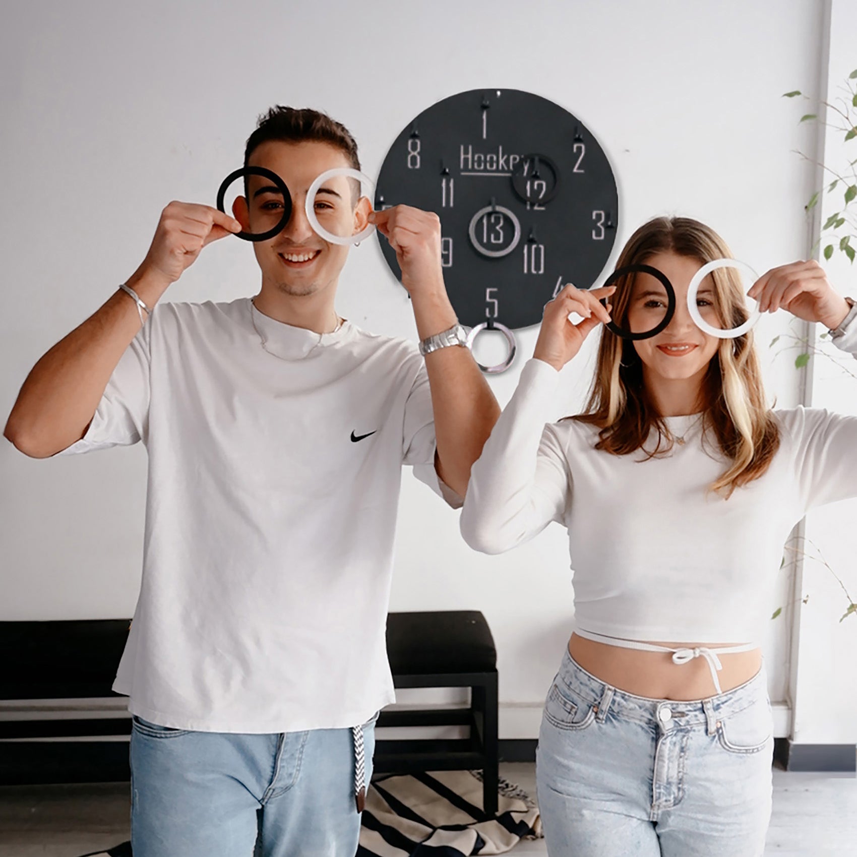 Two people holding black and white circular ring props for the hookey ring toss wall game for all age range