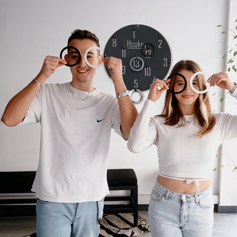 Two people holding black and white circular ring props for the hookey ring toss wall game for all age range