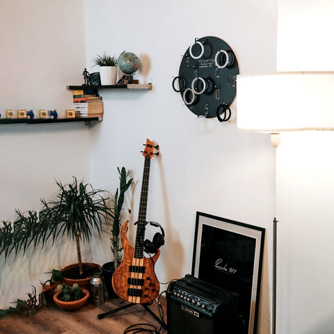 A wooden-finished bass guitar with natural wood grain and black hardware resting on a stand in a wall game setup