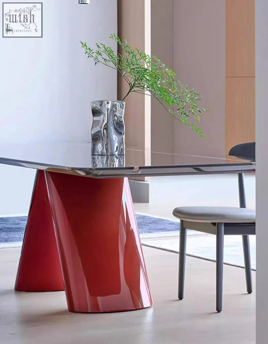 A sleek red hossain dining table with a modern sculpted base and a transparent glass marble dining top