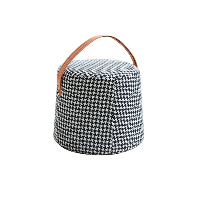 A houndstooth round footstool with black and white fabric and a tan leather handle for easy carrying