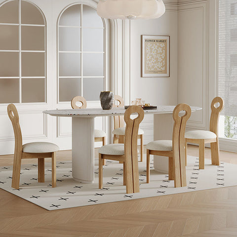 Modern white marble dining table with central pedestal base and light wood chairs with circular backrests