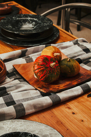 Three small colorful gourds with textured skins on a rustic wooden serving board next to a hygge black pasta bowl