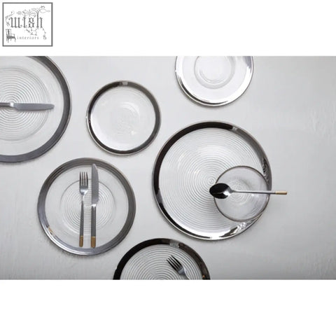 Set of modern glass coupe charger plates with silver rims and subtle concentric circular patterns