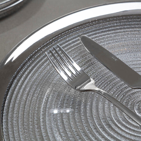 Shiny silver fork resting on ida embossed glass side plate with silver rim and textured embossed glass surface