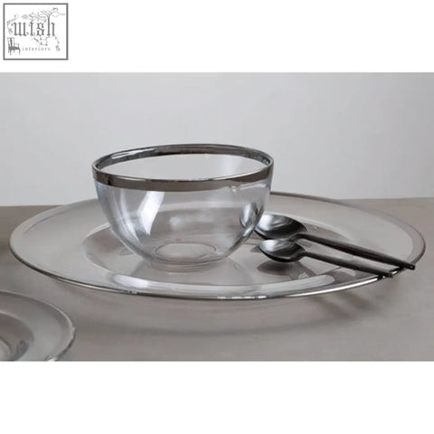 Clear glass bowl with silver rim on a matching ida glass charger plate with silver rim and two stainless steel spoons