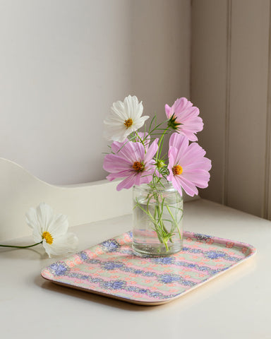 A clear glass jar with pink and white cosmos flowers on an ida wooden tray for decorative use