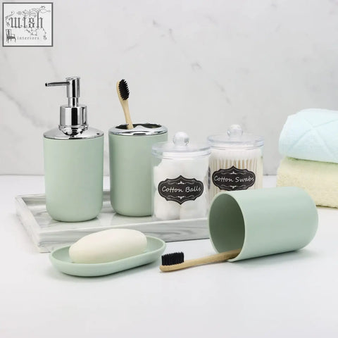 Mint green ceramic bathroom accessories set with chrome accents and labeled containers for soap, cotton, swabs, and toothbrushes