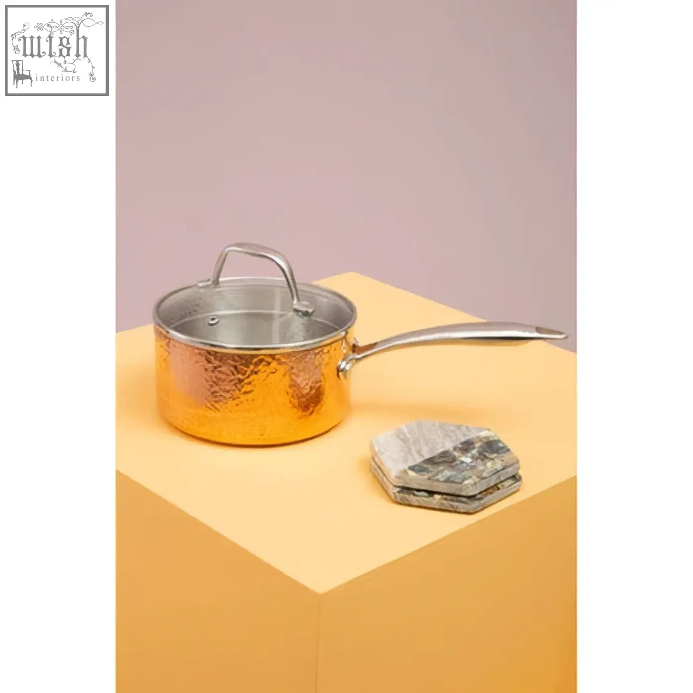 Golden hammered copper saucepan with stainless steel handle and lid shown with four beige marble and paua shell coasters