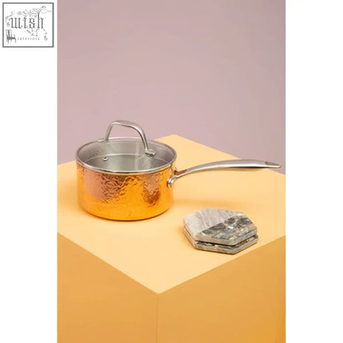 Golden hammered copper saucepan with stainless steel handle and lid shown with four beige marble and paua shell coasters
