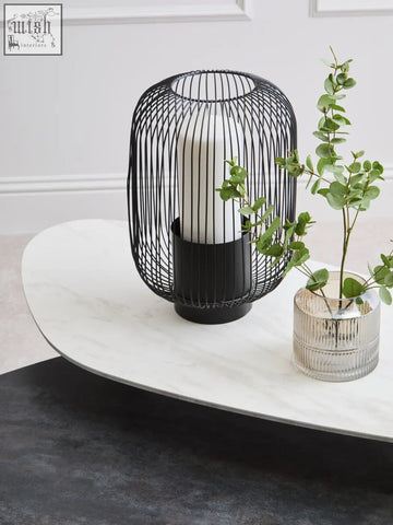 Black wireframe lantern with white candle on large asymmetrical ceramic coffee table for stylish home decor
