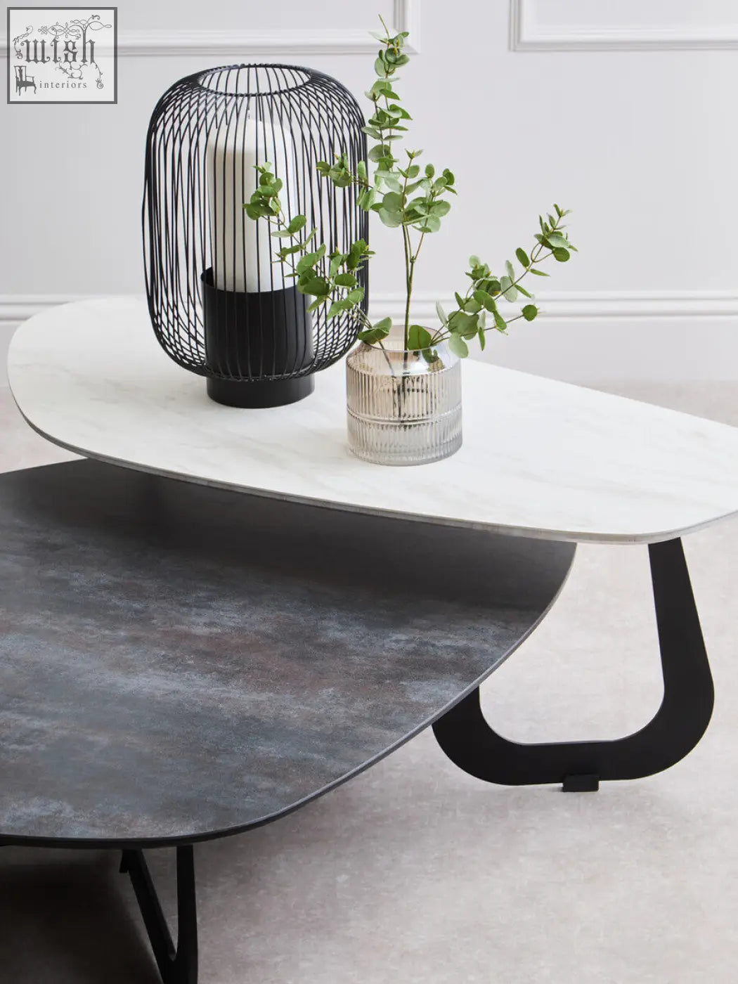 Modern black wire cage lantern with white candle on large asymmetrical ceramic coffee table with marble top