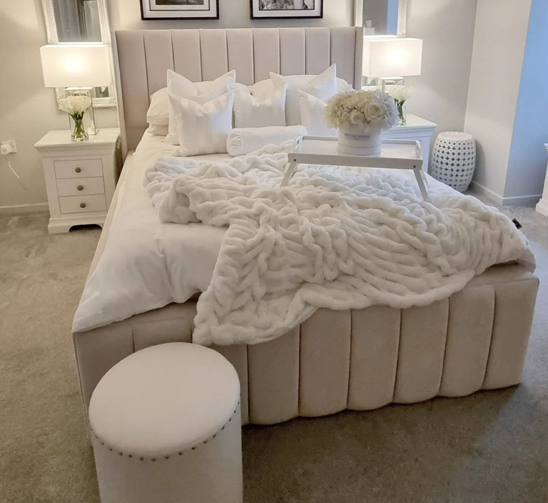 Cream-colored tufted indiana bed frame with upholstered headboard and footboard plus plush white knitted throw blanket