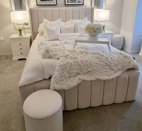 Cream-colored tufted indiana bed frame with upholstered headboard and footboard plus plush white knitted throw blanket