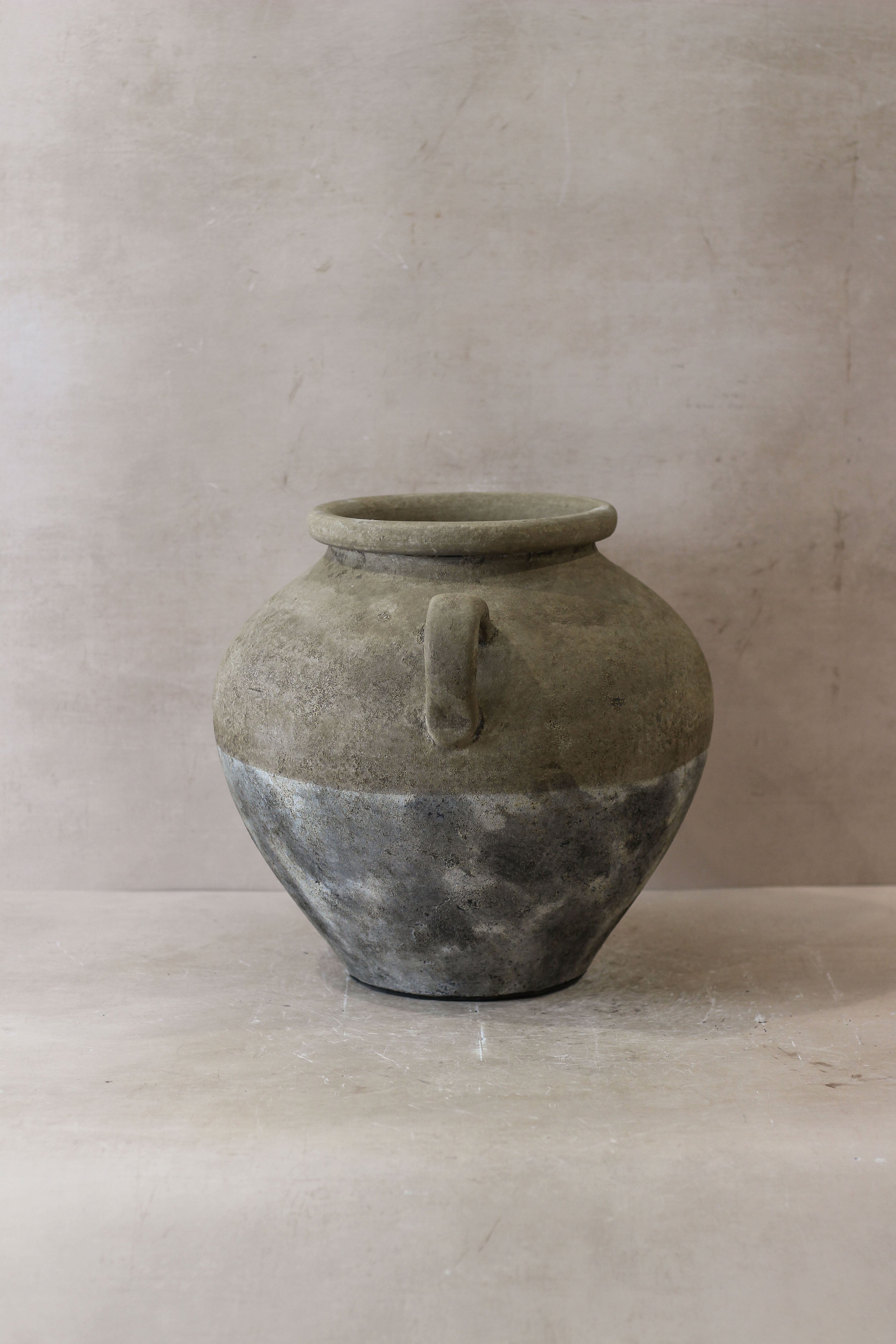 A rustic two-toned ceramic indonesia pot no 27 with a matte gray top and weathered darker bottom featuring a loop handle