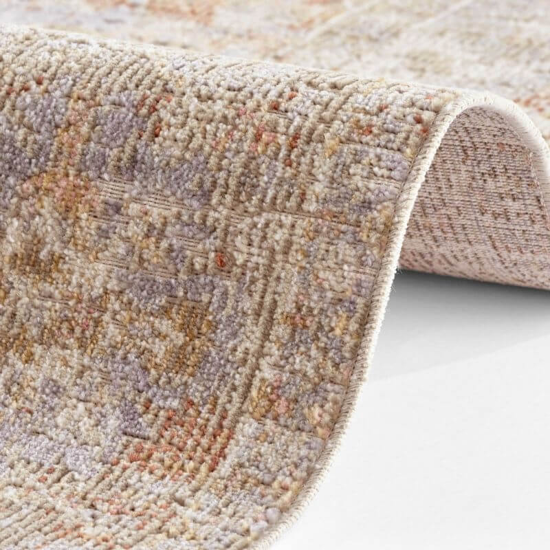 A soft indoor outdoor port said rug with a distressed medallion pattern in muted beige and dusty rose colors