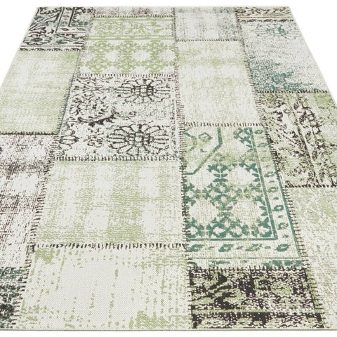 A patchwork indoor outdoor symi rug with faded green and black floral geometric patterns on an off-white base