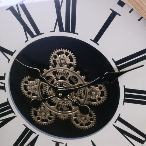 A white industrial large cog wall clock with black roman numerals and a metallic silver exposed gear mechanism