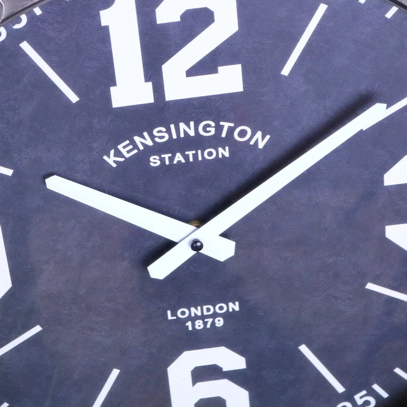 Dark blue industrial style wall clock with white numerals and hands featuring kensington station london 1879 text