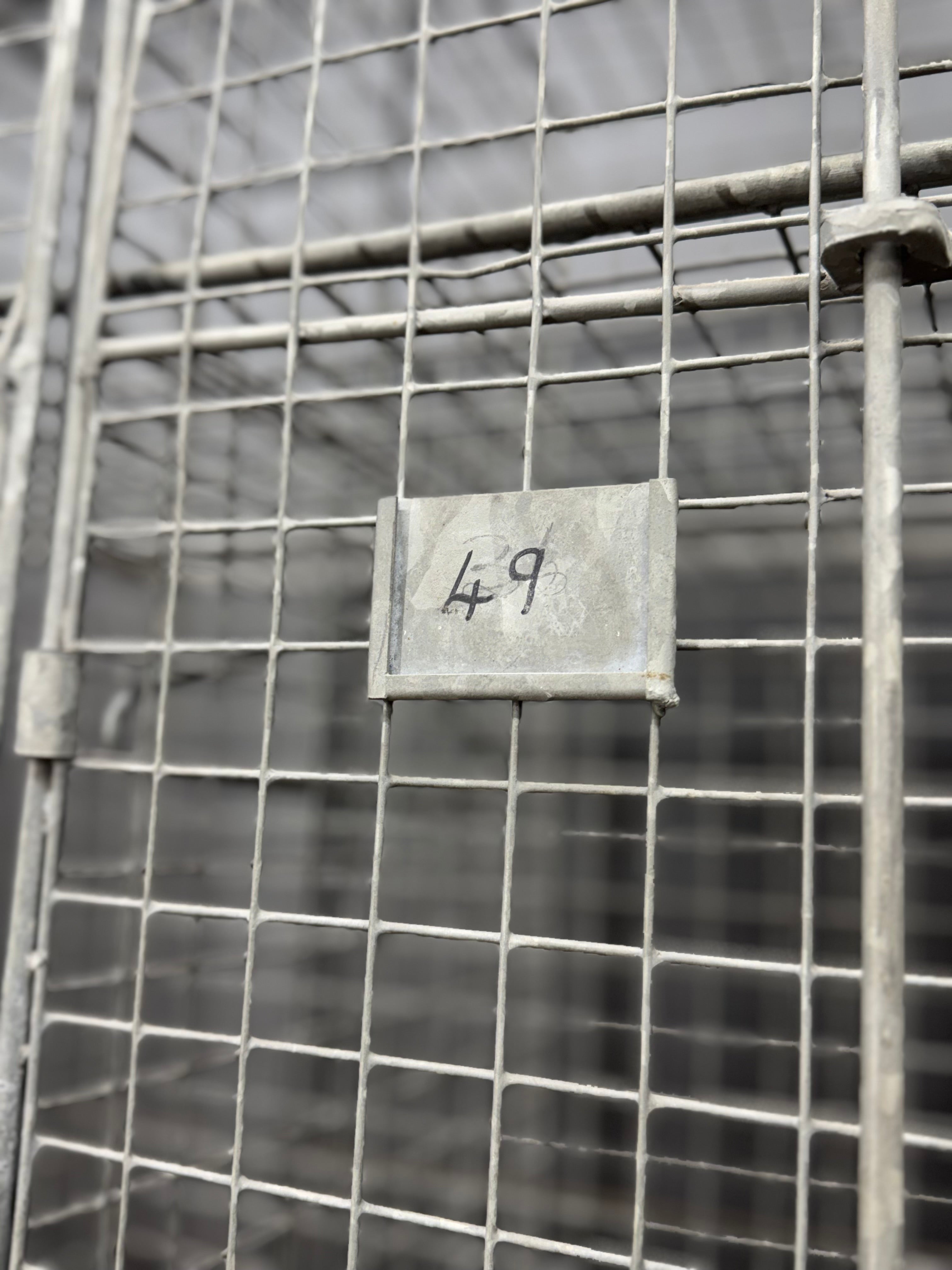Gray metal label with handwritten number 49 on a wire mesh door of an industrial vintage three door locker cabinet