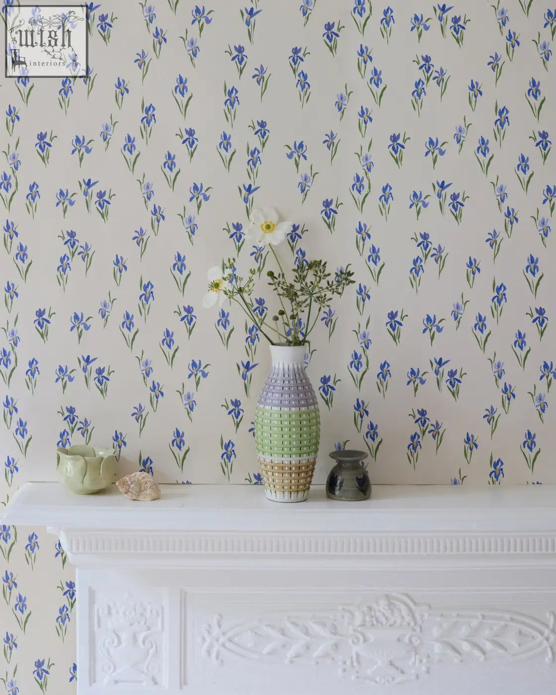 A tall slender vase with segmented pastel green and beige design complements blue floral iris wallpaper decor