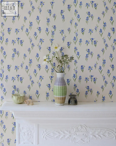 A tall slender vase with segmented pastel green and beige design complements blue floral iris wallpaper decor