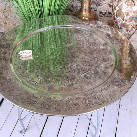 A round ornate brass moroccan tray table with intricate floral engravings and a reflective surface 80cm